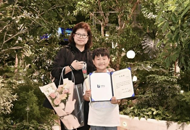 정태운 군과 정군의 어머니가 모범 어린이 표창장을 들고 환하게 웃고 있다.